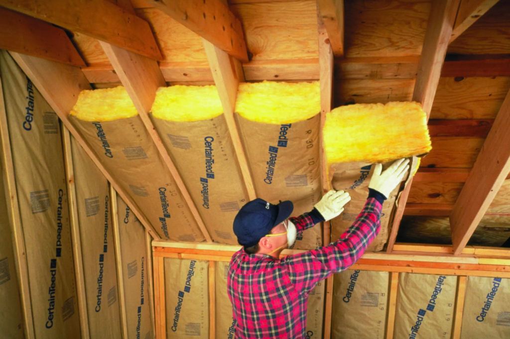 Contractor installing insulation between roof rafters in a home