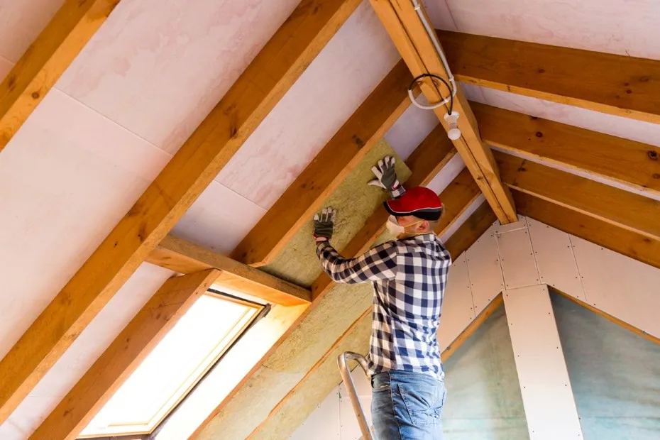 Contractor installing batt insulation along attic roof rafters